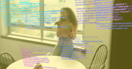 Talking developer woman holding smartphone, gesturing at wooden table by window, with floating code....