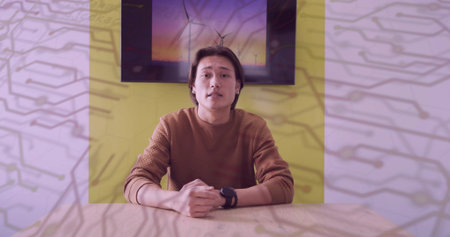 Presenting information Asian male sitting at wooden table in room with watch, wall-mounted display....