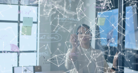 Sketching Asian woman drawing network diagrams on glass board in conference room, with white marker....