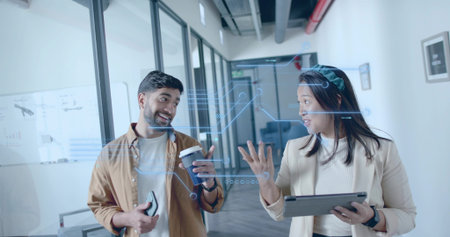 Walking coworkers in businesswear analyzing devices in office corridor, with floating graphics. Professional, collaboration, technology, corporate, workspace, modern, communicationの写真素材