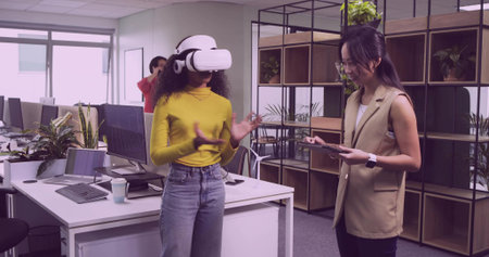 Gesturing co-worker wearing VR headset interacting with demo inside office, with tablet smartphone....