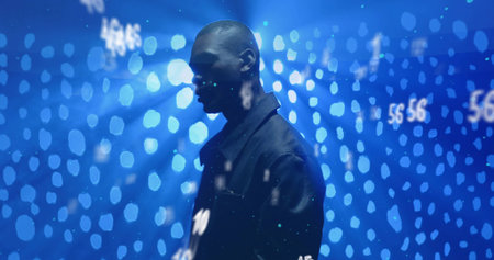 Standing man wearing dark jacket in dark studio, with blue bokeh lights and numeric projections. Technology, futurism, innovation, digital, data, virtual, minimalismの写真素材