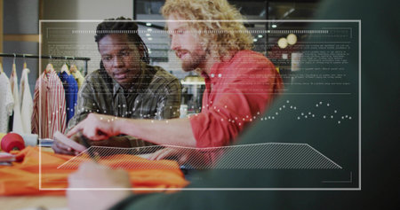 Reviewing designers analyzing garments in studio with tablet, orange fabric and digital overlays. Fashion, collaboration, innovation, technology, retail, style, creativityの写真素材