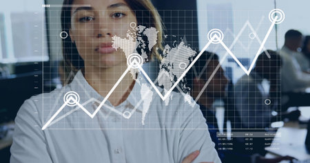 Standing woman wearing white shirt crossing arms in office, with monitors displaying data overlay. Professional, collaboration, technology, analytics, business, strategy, modernの写真素材