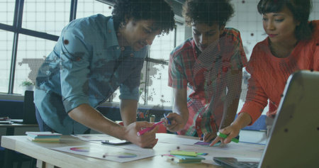 Coworkers collaborating in open office, pointing at pie charts and bar graphs with sticky notes....
