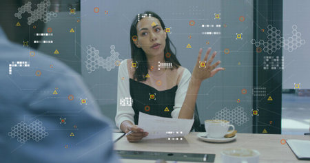 Gesturing woman presenting documents at table in meeting room, with coffee cup and digital overlay. Collaboration, innovation, professionalism, modernity, communication, strategy, teamworkの写真素材