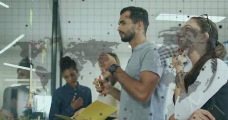 Man in gray shirt holding markers at office glass partition, with world map and sticky notes....