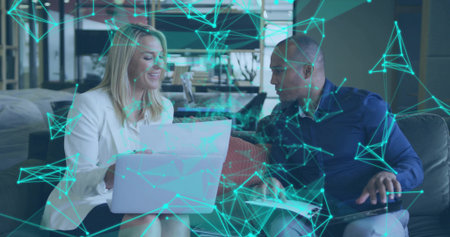 Examining documents on laptop in coworking lounge, woman in white blazer and man under teal overlay....