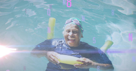 Floating senior swimmer holding yellow pool noodle in outdoor pool, wearing swim cap, pink goggles....