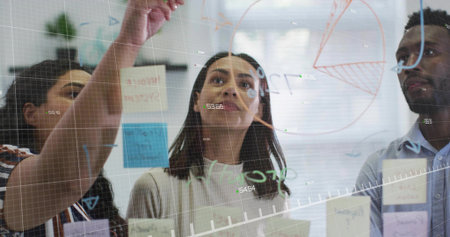 Brainstorming business professionals writing on glass board in office boardroom, with sticky notes....