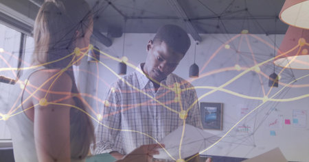 Reviewing papers coworkers wearing casual attire discussing data in office with network overlay....
