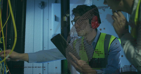 Male engineer with vest holding clipboard in data center rack, colleague adjusting patch cables....