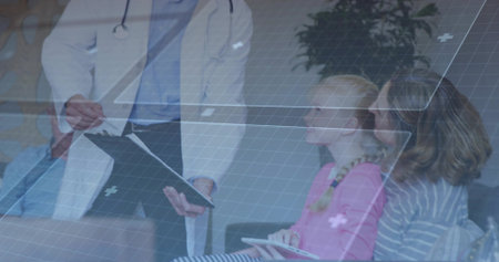 Consulting doctor in white coat engaging mother and daughter at clinic with wheelchair and tablet....