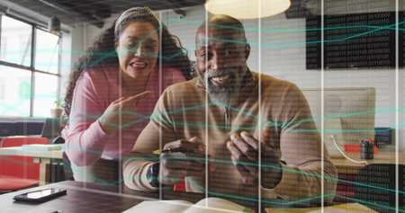 Holding smartphone senior tech and woman coworker reviewing code at office desk with open notebook. Collaboration, innovation, teamwork, digital, professional, modern, communicationの写真素材