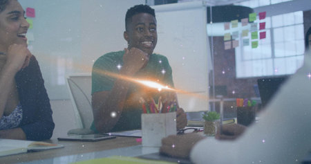 Gesturing man in green tee discussing in office, with notebooks smartphone glass wall sticky notes....
