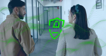 Walking coworkers viewing green data overlay with shield-camera icon in glass corridor with phone....