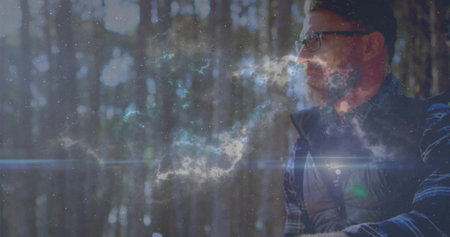 Sitting man gazing ahead in pine forest, with quilted vest, plaid shirt, eyeglasses, copy space. Solitude, tranquility, nature, reflection, mystical, bohemian, scenicの写真素材