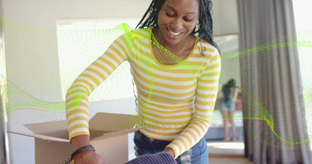 Unpacking woman in striped top and jeans lifting folded fabric from box at home, with mirror....