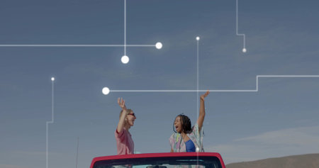 Driving red convertible, two women raising arms on rural road under blue sky. Adventure, friendship,...