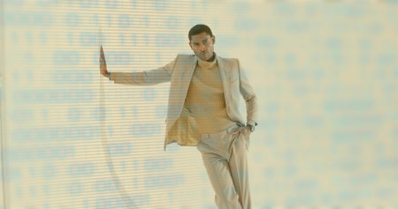 Leaning male model wearing beige suit pushing palm forward in studio, with binary code overlay. Professional, fashion, sleek, innovation, digital, modern, businessの写真素材