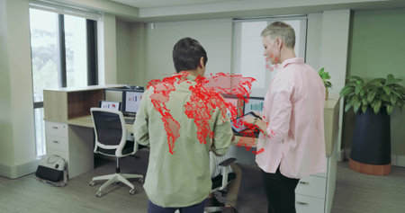 Collaborating colleagues in button-up shirts reviewing tablet in modern office, with dual monitors....