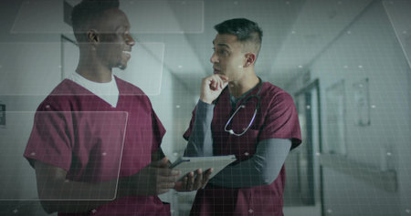 Gesturing toward tablet two medical staff discussing data in hospital hallway, with stethoscope....
