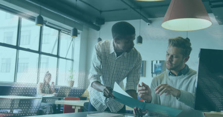 Discussing two male office workers reviewing blue folder in open-plan office, with grid windows. Collaboration, teamwork, productivity, modern, workspace, innovation, professionalの写真素材