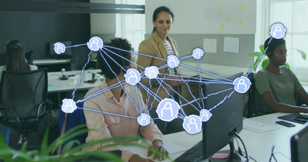Typing team collaborating in open plan office, with monitors tablet headphones blazer network icons....