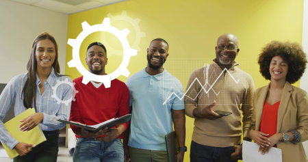Collaborating team of five showing data graphic by yellow wall in office holding papers and devices....