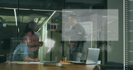 Three professionals discussing and pointing bar chart in glass-walled room, with laptop and papers....