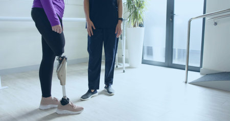 Woman in purple top with prosthetic leg practicing standing using parallel handrails in rehab room. Rehabilitation, therapy, mobility, recovery, strength, resilience, wellnessの写真素材