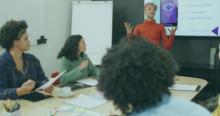 Gesturing Asian presenter wearing red sweater toward display screen at conference table, copy space....