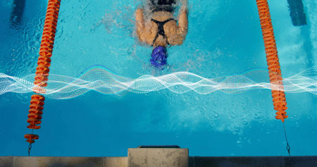 Gliding female swimmer wearing black swimsuit and blue cap through pool lane, with orange dividers....