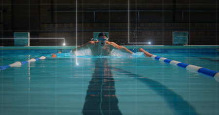 Performing butterfly stroke swimmer wearing swim cap, goggles in lane center, with lane dividers. Athlete, aquatic, sport, training, competition, aquatic facility, fitnessの写真素材