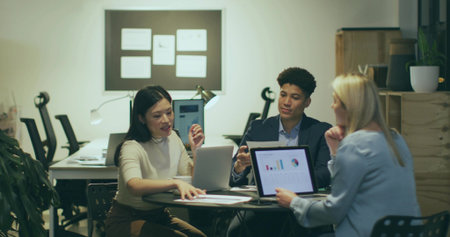 Collaborating three professionals in suits reviewing documents at office table, with laptops. Collaboration, teamwork, business, startup, professional, office, strategyの写真素材
