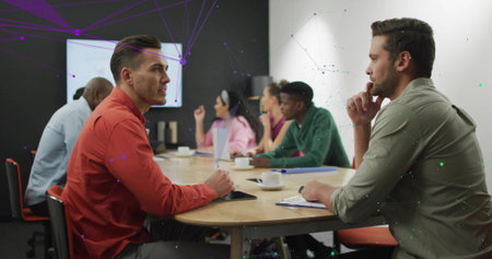 Discussing colleagues in pink, blue, green attire around oval table in office with network graphics....