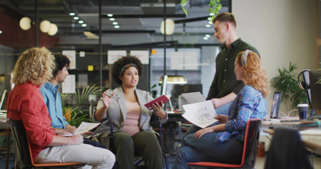 Leading woman in wheelchair in business attire presenting charts in open office, with sticky notes. Collaboration, teamwork, diversity, innovation, interior, modern, productivityの写真素材