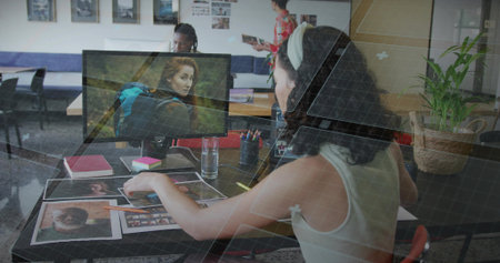 Arranging professional wearing tank top sorting photographs at studio desk, with computer monitor. Creative, teamwork, modern, collaboration, artistic, workspace, innovationの写真素材