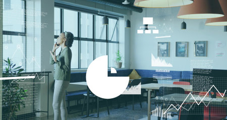Talking woman wearing business casual holding smartphone at office lounge, with tables and plants....
