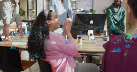 Clapping adult woman in pink cardigan laughing by wooden desk in modern office with monitor....