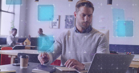 Typing mid adult male wearing grey sweater at shared office desk, with laptop smartphone coffee cup. Collaboration, coworking, architecture, teamwork, productivity, modern design, communicationの写真素材