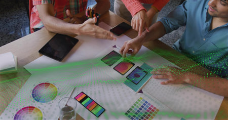 Collaborating design team reviewing phone mockups in design studio, with color wheels and swatches. Creative, teamwork, innovation, visual, vibrant, brainstorming, modernの写真素材