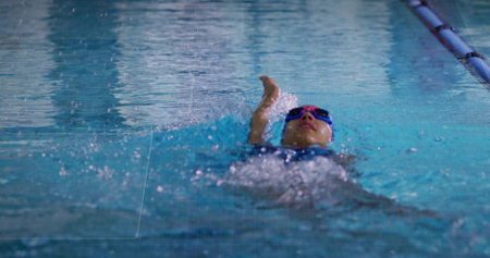 Swimmer wearing blue swimsuit pink cap and goggles performing backstroke in pool, with lane divider. Athlete, competition, aquatic, fitness, determination, exploration, motionの写真素材
