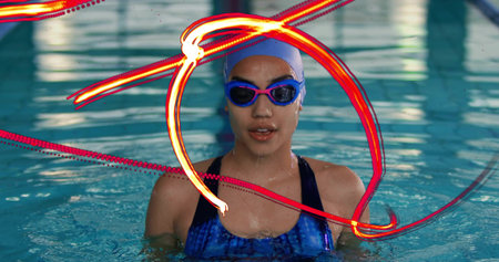 Emerging swimmer wearing swimsuit lifting torso over water at pool, with swim cap and goggles....