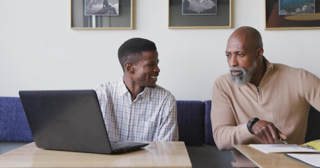 Pointing man wearing beige sweater reviewing documents smiling at colleague in office, with laptop. Collaboration, teamwork, professional, modern, office, discussion, leadershipの写真素材