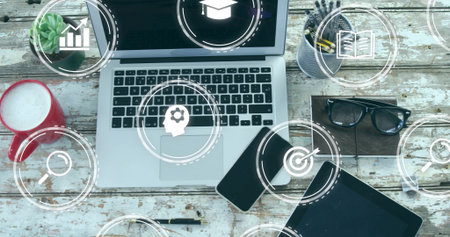 Presenting laptop showing digital overlay icons at study desk with coffee mug, gadgets, accessories. Technology, innovation, workspace, productivity, modern, design, educationの写真素材