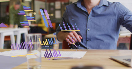 Reviewing man in blue shirt manipulating digital bar charts at office desk, with printed documents. Technology, innovation, data, analytics, workspace, collaboration, modernの写真素材