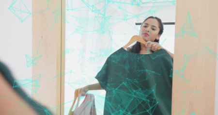 Indian woman comparing dark top and light garment in dressing room, with full-length mirror. Clothing, fashion, retail, wardrobe, minimalism, styling, interiorの写真素材