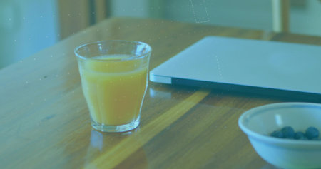 Orange juice glass sitting on wooden dining table at home, with laptop, blueberry bowl, copy space. Rustic, minimalist, productivity, casual, natural, fresh, cozyの写真素材