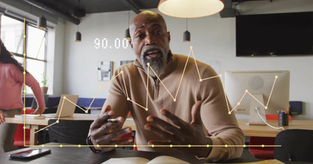 Gesturing mature African American man displaying graphs at coworking office, with computer monitor....